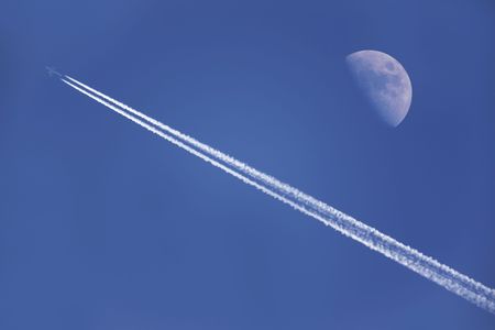 An airplane flying near the moon in the afternoonの写真素材