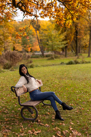 Beautiful young woman sitting on a bench in the autumn park.の写真素材