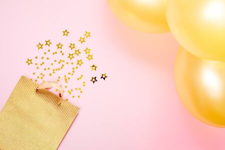 Valentines Day background concept. Sweet holiday background with a golden paper gift bag, small stars and gold Balloon on pink paper background.の写真素材