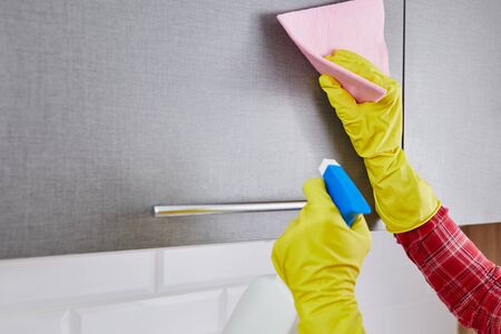 woman in protective gloves with spray cleaning gray kitchen cabinet
