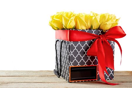 Flowers in a box with red ribbon bow on wooden table. Bouquet of yellow roses. Valentines day concept.の写真素材