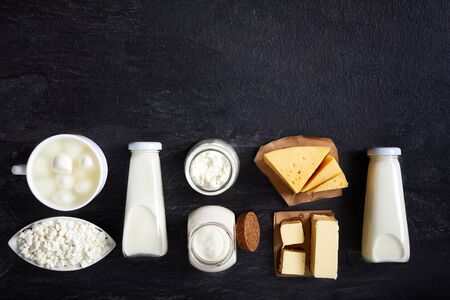 top view of dairy products on a dark background. Milk, sour cream, mozzarella, kefir, yogurt, butter, cheese assortment.の写真素材
