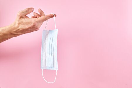 Hand holding medical protective mask on pink background