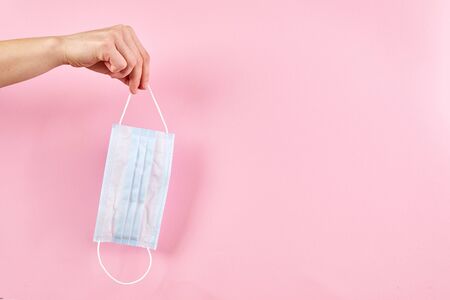 Hand holding medical protective mask on pink background