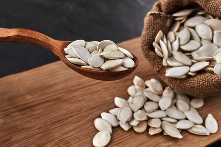Pumpkin seeds and a wooden spoon on a dark table. Cutting board and canvas bag . Copy space. close...