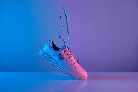 Trendy white teenage sneakers with flying laces in trendy neon light. New shoe in retro surreal red, blue gradient light, Close upの写真素材