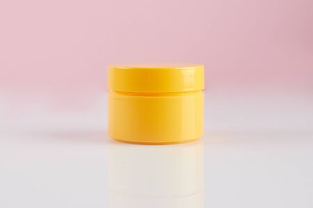 Jar of moisturizing facial cream. Yellow plastic container with cream on a pink background.の写真素材