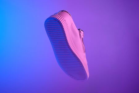 Trendy white teenage sneakers flying in trendy neon light. Levitation Shoes in red, blue light. Creative minimalism. Close upの写真素材