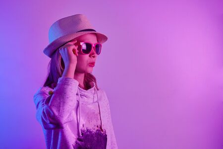 Teen girl in sunglasses standing and surprised over trendy blue neon light. Portrait of millennial pretty teenager.の写真素材
