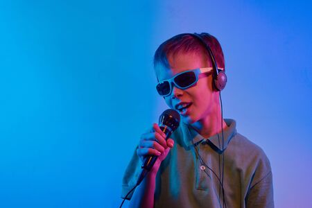 Caucasian teen boy portrait on blue neon light. Male model with microphone. Concept of human emotions, music, art.の写真素材