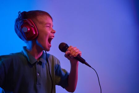 Caucasian teen boy portrait on blue neon light. Male model with microphone singing karaoke.の写真素材