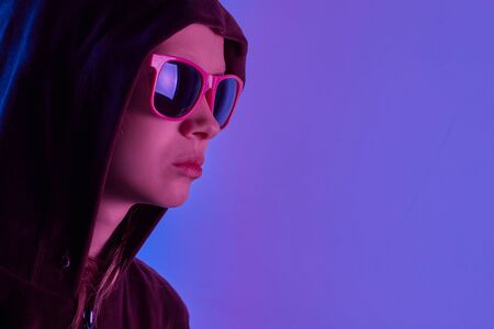 Teen girl in sunglasses posing over trendy blue neon light. Portrait of millennial pretty teenager....