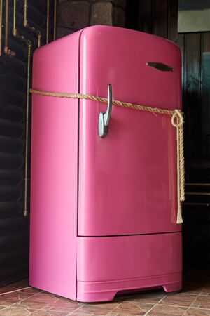 Closed pink refrigerator tied with a rope. A locked fridge as concept of food restrictions or diet.の写真素材