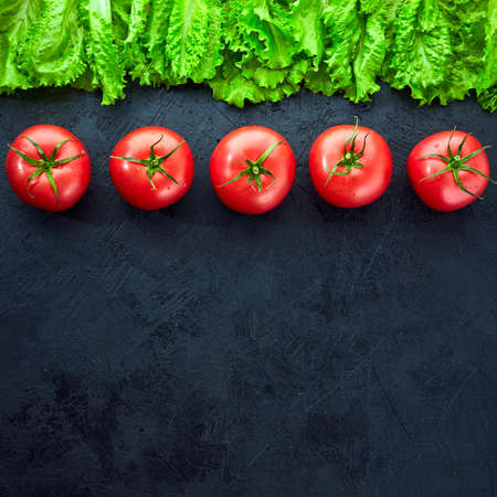 Fresh grape tomatoes with salad Leaves on black stone background. Vegan veggies diet food. Herb, tomatoes, cooking concept.の写真素材