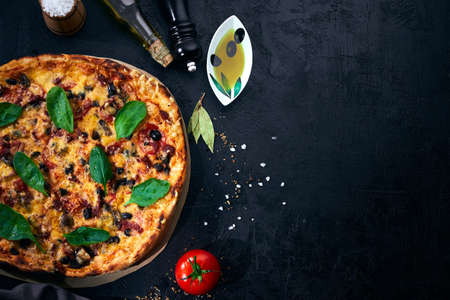 Italian pizza and pizza cooking ingredients on dark background. Tomatoes, olives oil, herbs and spices.の写真素材