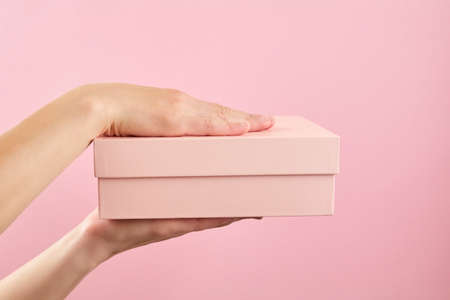Woman hand hold the pink box on pink wall background. Concept of parcel deliveryの写真素材