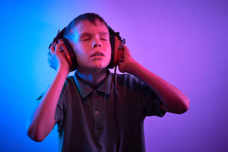Teenager listening music with headphones in trendy neon light. Portrait millennial pretty boy.の写真素材
