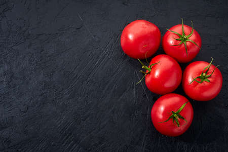 Ripe tomatoes on a dark stone background. Culinary image of fresh tomatoes ready to cook.の写真素材