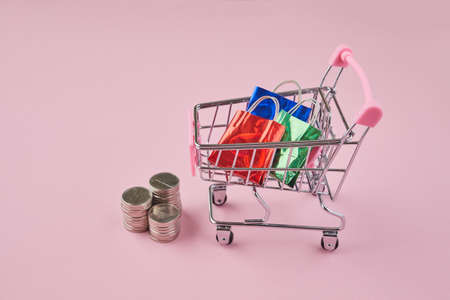 Shopping in trolley with bags on a pink background. Trolley cart and colorful paper shopping bags.