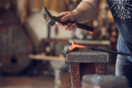 Blacksmith manually forging on iron on anvil at forge. Treatment of molten metal close-up.