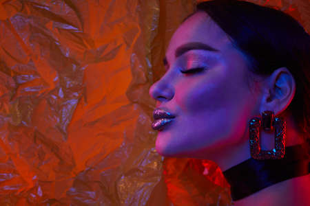 Woman with metallic silver lips in neon lights in studio with transparent film on background. Art make up.の写真素材