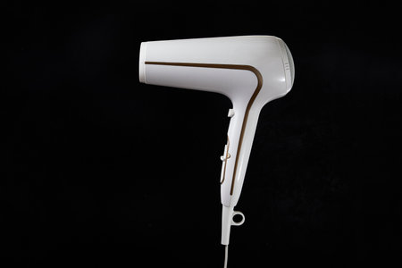 Professional stylish hairdryer isolated over a black background. White Ionic Hair Dryer with Hair...