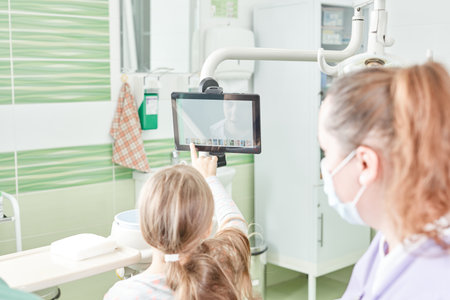 Dentist with protective mask and child pointing at the screen in stomatology office.の写真素材