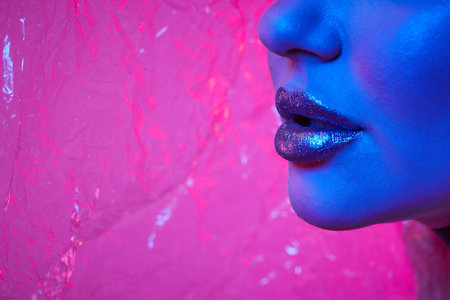 Woman with metallic silver lips in neon lights in studio with transparent film on background. Art make up.の写真素材