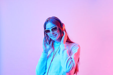 Fashion pretty girl with headphones listening to music on neon background at studio. Smiling woman.の写真素材