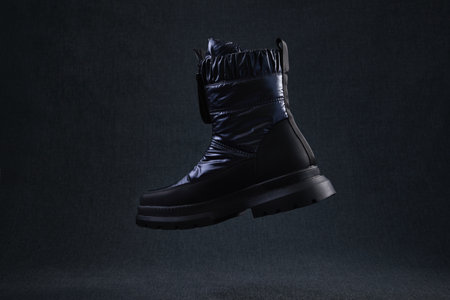 Fashion black unbranded boot flying on dark background. Black winter walking shoes levitate in air....