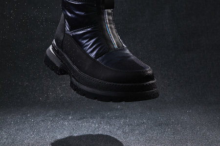 Fashion black unbranded boot with drops, spray and splashes flying on dark background. Modern female...