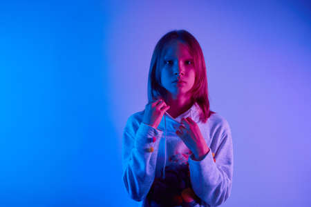 Teen girl standing and posing over trendy blue neon light. Portrait of millennial pretty teenager....