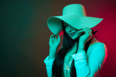 Sexy young woman on colorful background. Brunette model girl in sexy clothes and hat in neon light.