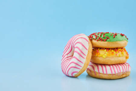 Donuts glazed with sprinkles on pastel blue background. Sweet donuts on blue paper. Close up.の写真素材