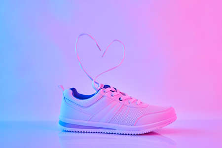 Sports sneakers with heart-shaped laces in neon light. Concept of Love and Valentine's Day.の写真素材
