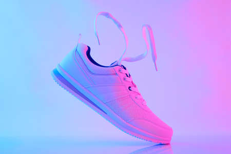 Fashion white sneakers in neon light. Sport shoes for training in the gym. Creative minimalism.