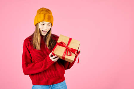 Young smiling happy hipster girl with baces holding present boxes celebrating new year, wearing red...