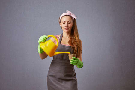 Beautiful young housewife watering the flowers or seedling in pots in studio. Woman gardener waters plants from watering can. Making domestic work.の写真素材