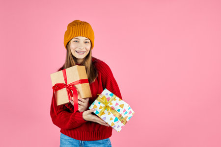 Young smiling happy hipster girl holding present boxes celebrating new year, wearing red knitted...