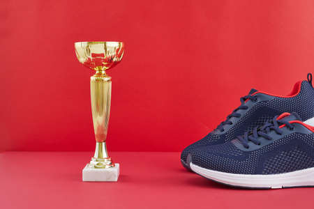 Golden trophy and running shoes on a red background. Winner in sport competition. Footwear and golden award trophy.の写真素材