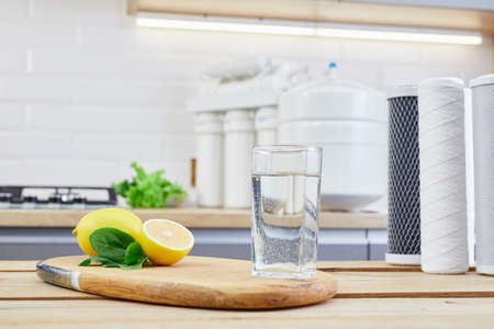 Glass of filtered clean water with reverse osmosis filter, lemons and cartridges on a table in kitchen. Concept Household filtration or purification system.の写真素材