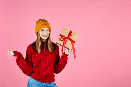 Young smiling happy hipster girl holding present boxes celebrating new year, wearing red knitted...
