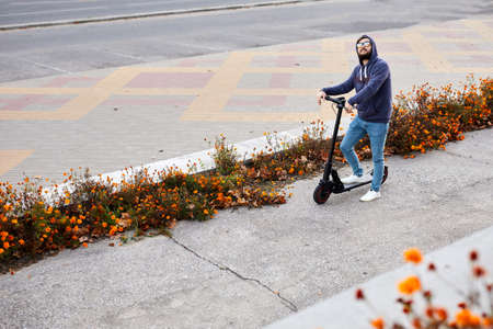 Bearded stylish man riding the electric scooter. Guy on daily commute riding micro scooter.の写真素材