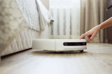Female hand switching on robotic vacuum cleaner at home. Woman using automatic robotic vacuum cleaner in living room.の写真素材