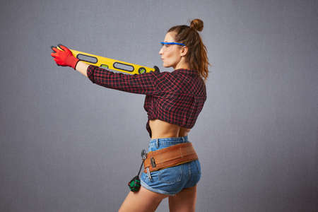 Sexy longhaired woman in casual clothes protective gloves hold spirit level in hand. Studio...