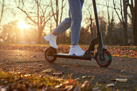 Young woman discover city and park at sunset with electric scooter or e-scooter. Female Legs in...