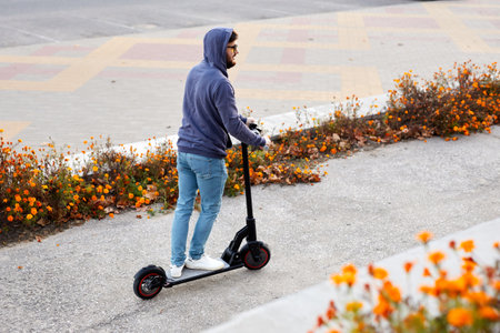 Bearded stylish man riding the electric scooter. Guy on daily commute riding micro scooter. Male in...