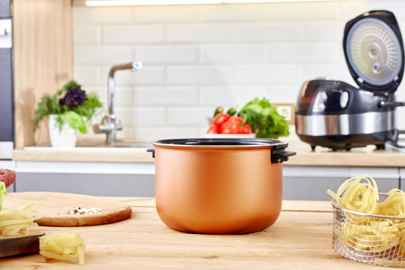 Cutting board with vegetables and multicooker on table in a modern kitchen. Electric crockpot and food at home kitchen. Automatic slo-cooker.の写真素材