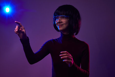 Woman with a smile touches the air in virtual reality glasses. A hand on a bright background points...