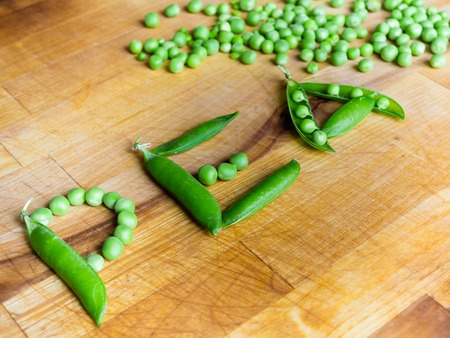 Word PEA created with peas on a wooden board with a podded peas in the backgroundの写真素材